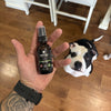 Hand holding a bottle of natural sleep spray with a dog in the background on a wooden floor.